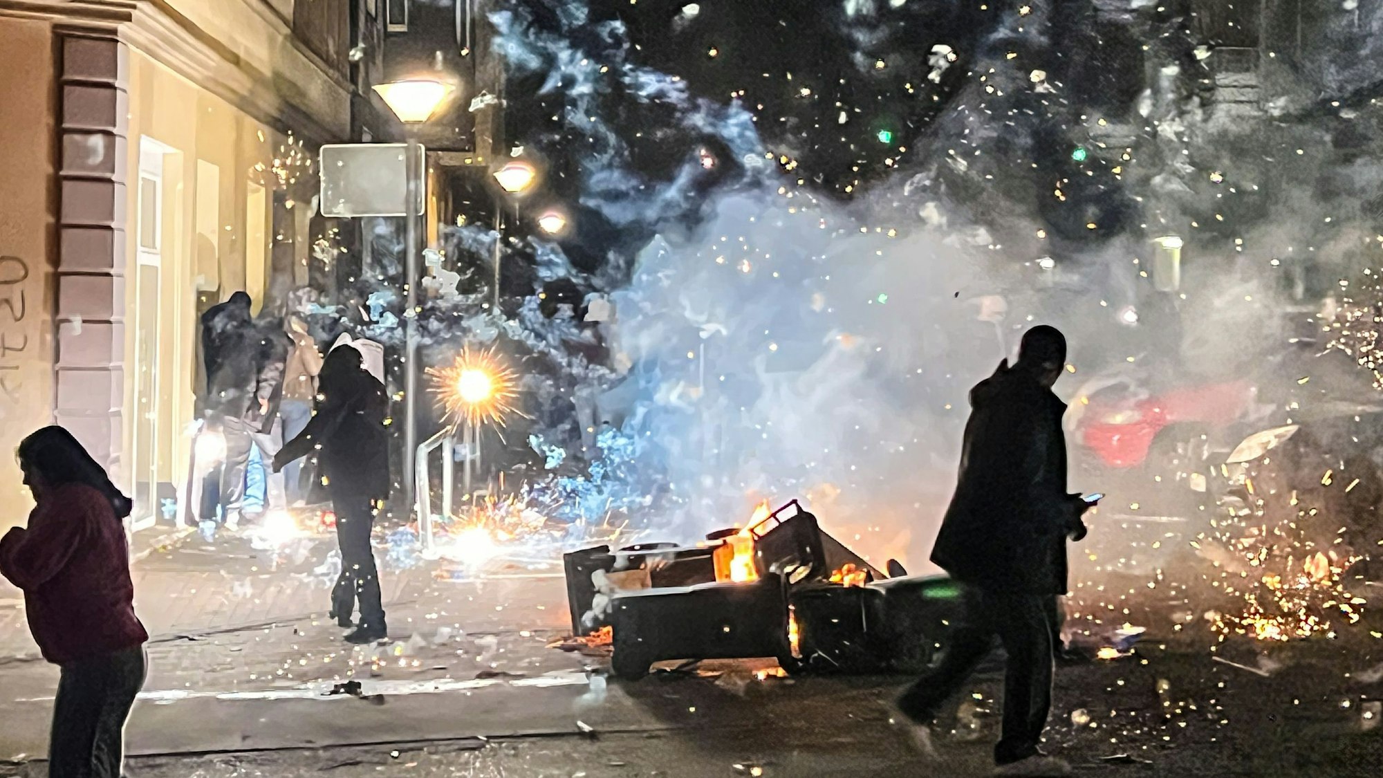 Ausschreitungen in der Silvesternacht: Vermummte Randalierer errichten mit Mülltonnen, Waschmaschinen und Sperrmüll brennende Barrikaden – Streifenwagen werden mit Glasflaschen und Feuerwerk beworfen.
