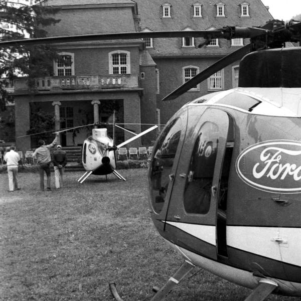 Zwei Hubschrauber mit Ford-Logos steht vor der Burg Dalbenden, daneben drei von der Kamera abgewandte Personen. Das Foto ist in schwarz-weiß.