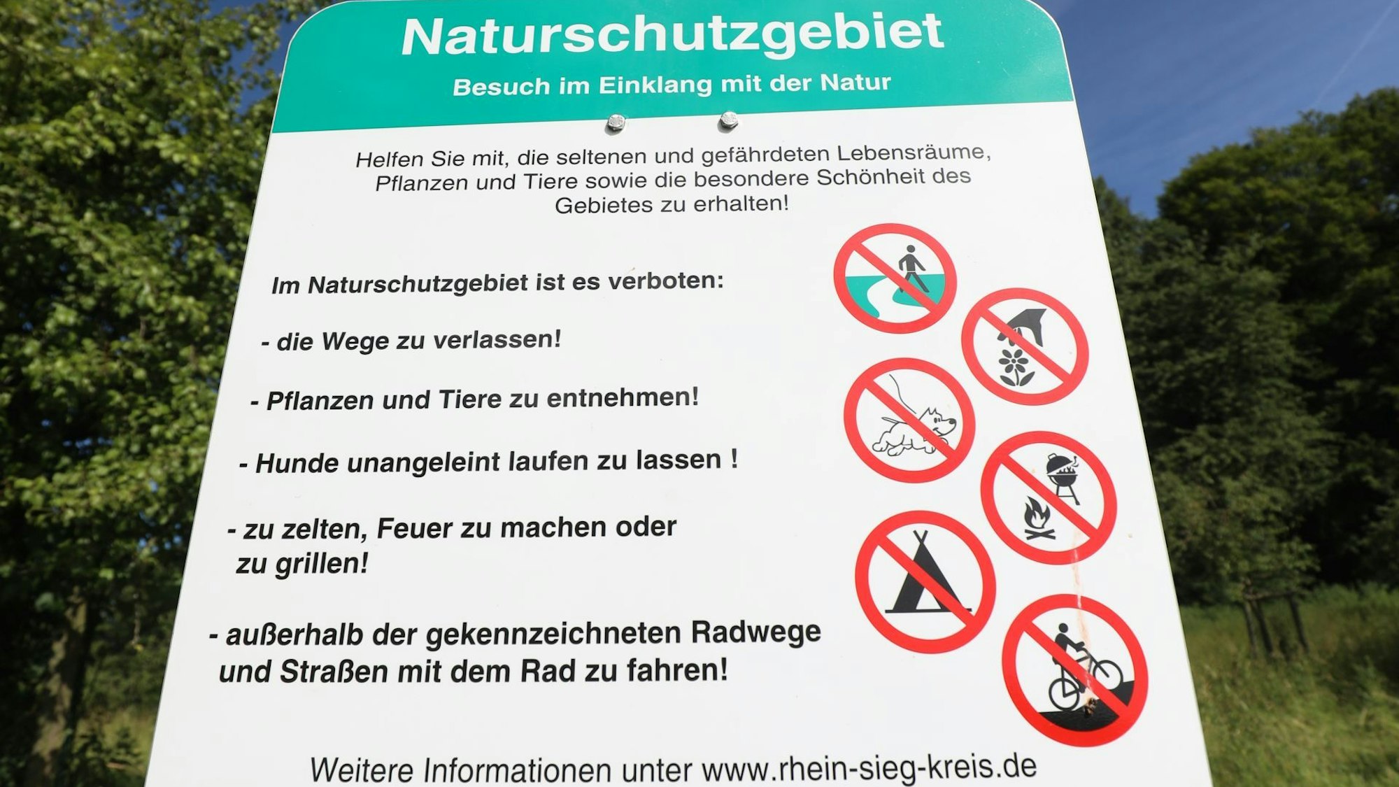 Ein Schild zeigt rot-weiße Piktogramme, mit denen Verbote wie Zelten oder das Verlassen der Wege bildlich gemacht werden.
