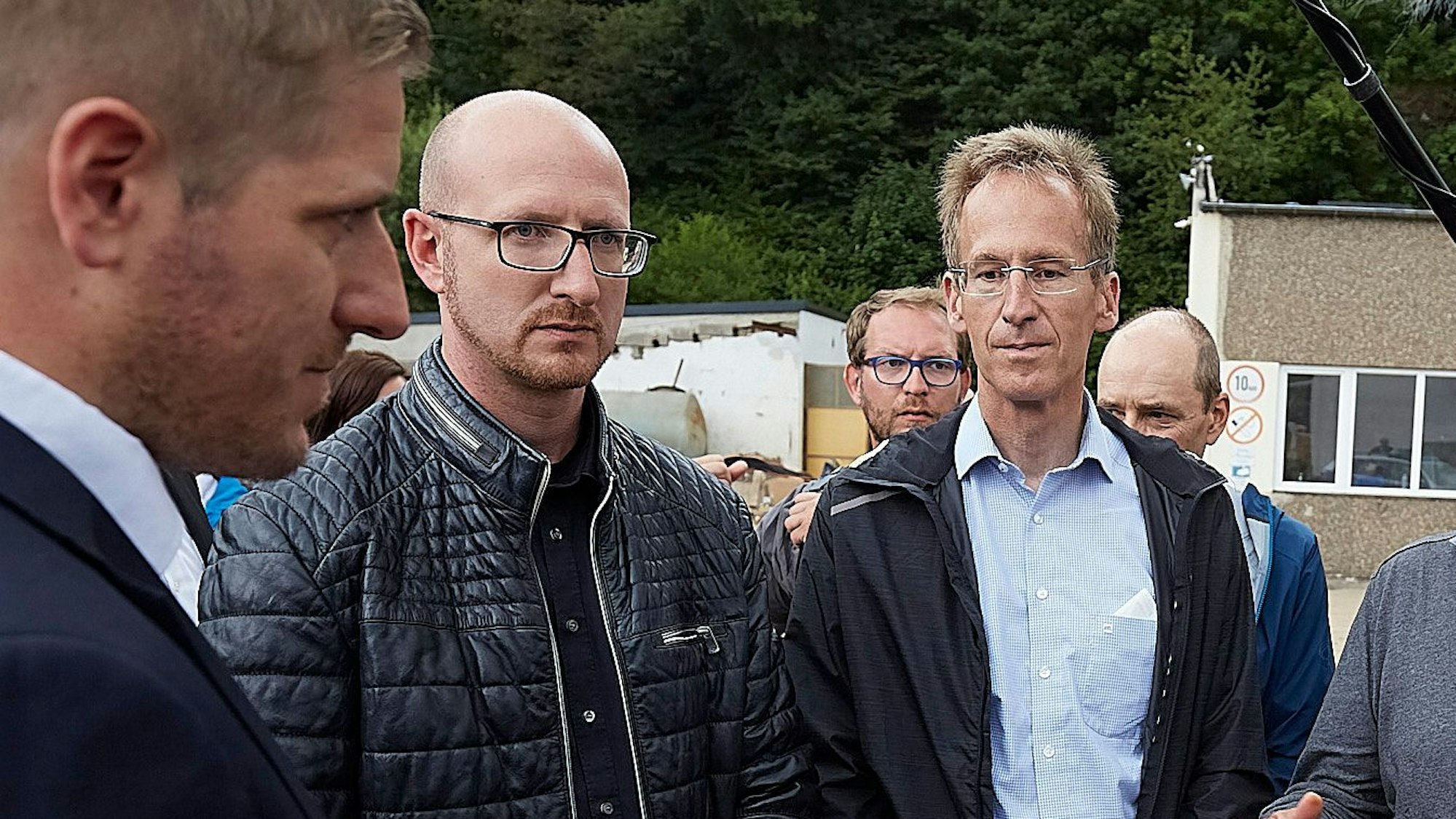 Drei Männer stehen mit ernsten Mienen zusammen.