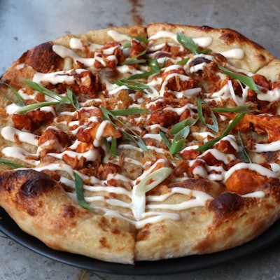 Eine vegane Pizza des Restaurants „Virtuous Pie“ liegt verzehrbereit auf einem schwarzen Teller.