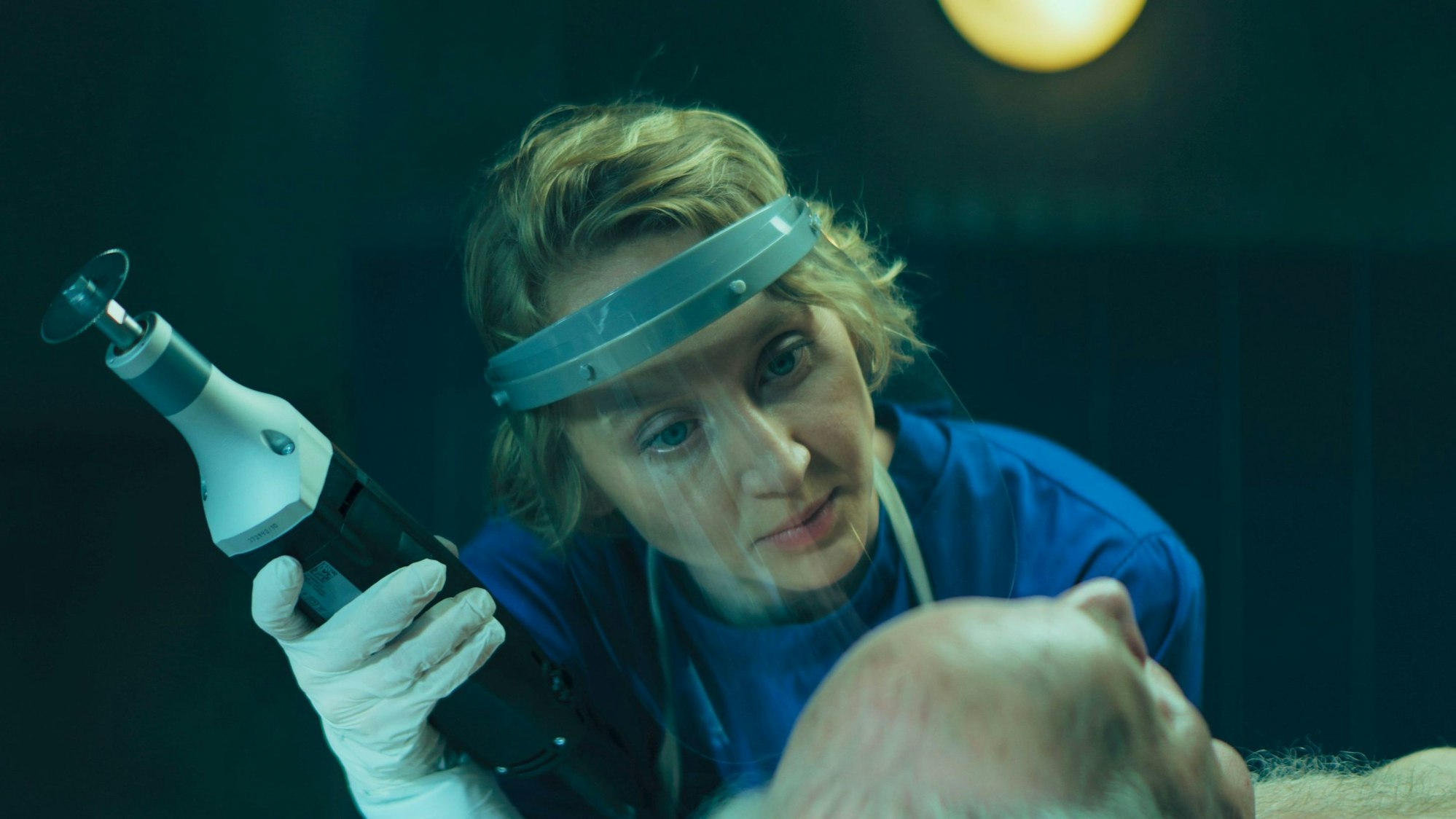 Bestatterin Blum, gespielt von Anna Maria Mühe begutachtet eine Leiche und hält in Seziergerät in den Händen.