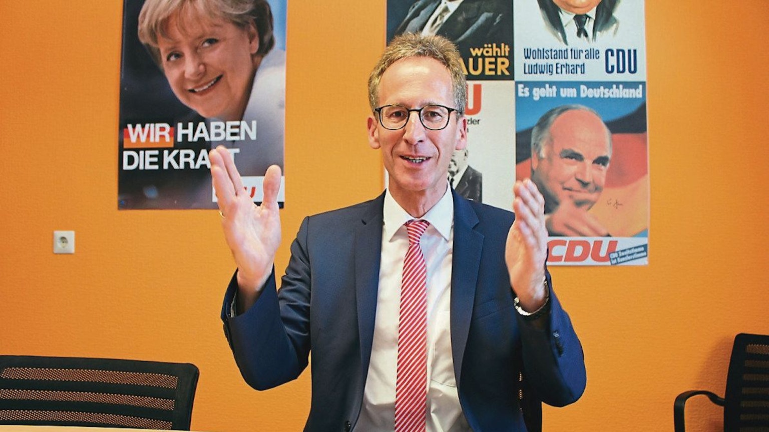 Detlef Seif sitzt am Tisch, an der Wand hängen alte CDU-Wahlplakate mit Angela Merkel und Helmut Kohl.