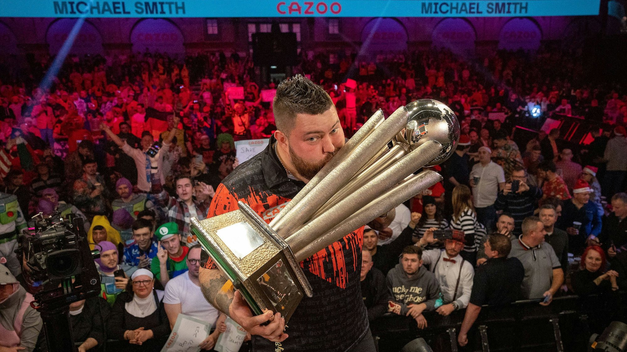Michael Smith küsst auf der Bühne des Alexandra Palace die WM-Trophäe.