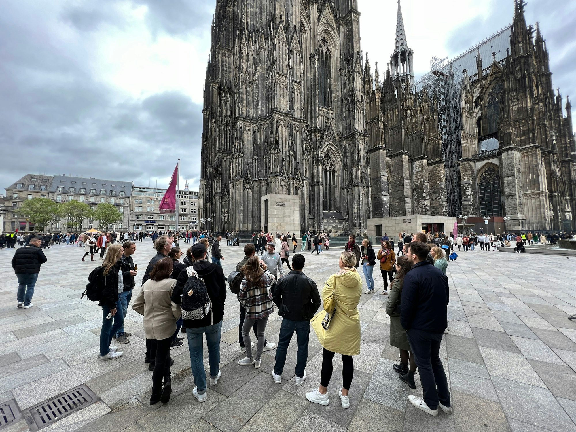 Matthias Boden steht vor dem Kölner Dom und erzählt einer Free Walking Tour Gruppe Fakten über den Dom.