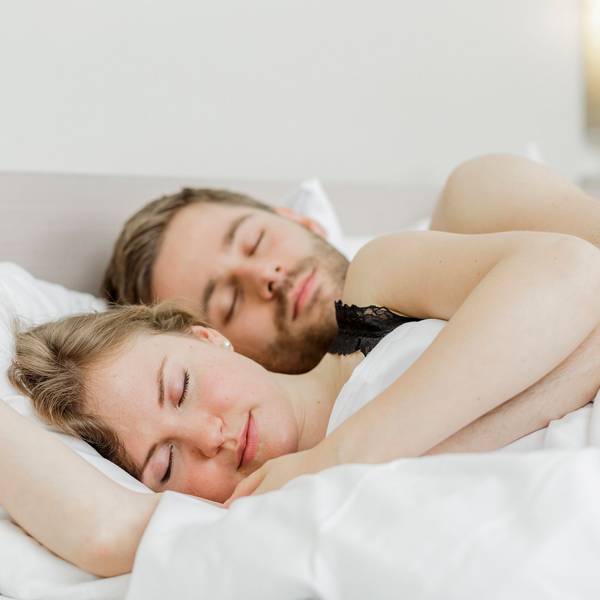 Eine Frau und ein Mann liegen aneinandergekuschelt im Bett und schlafen.