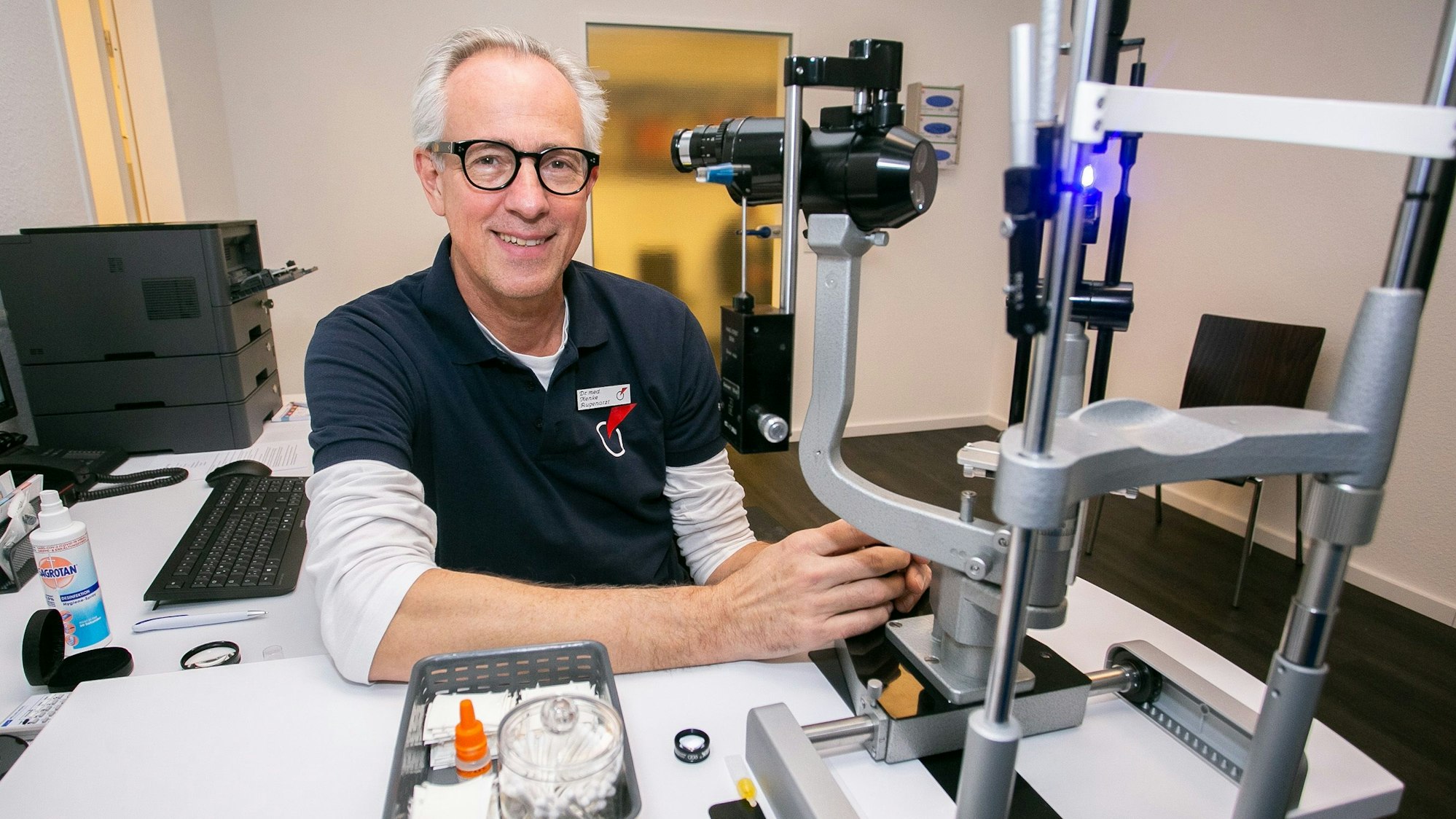 Augenarzt Dr. Ludger Henke sitzt vor einem Augenmessgerät für Patienten.