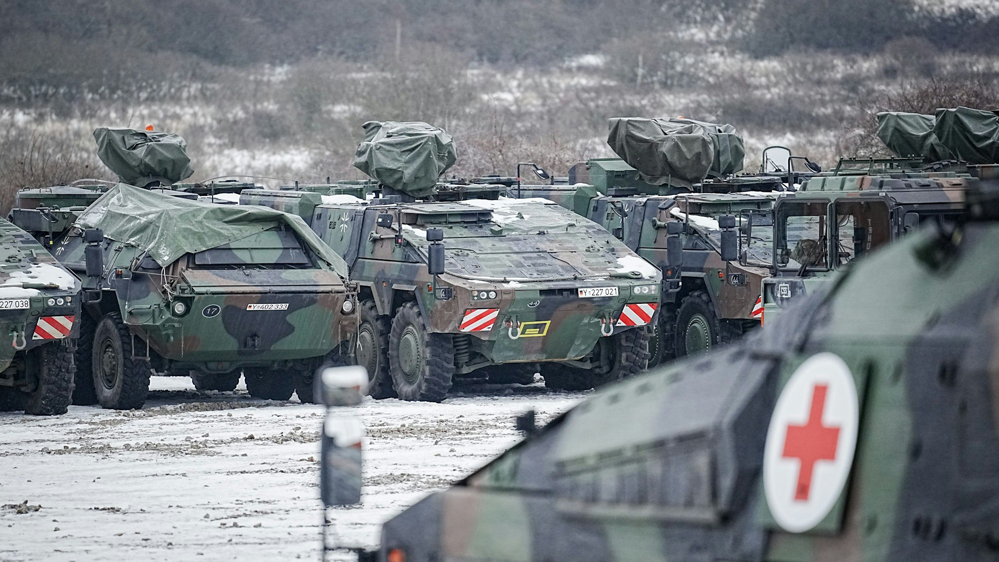 Truppentransportpanzer vom Typ Boxer und Radpanzer vom Typ GTL stehen in einem schneebedeckten Feldlager.
