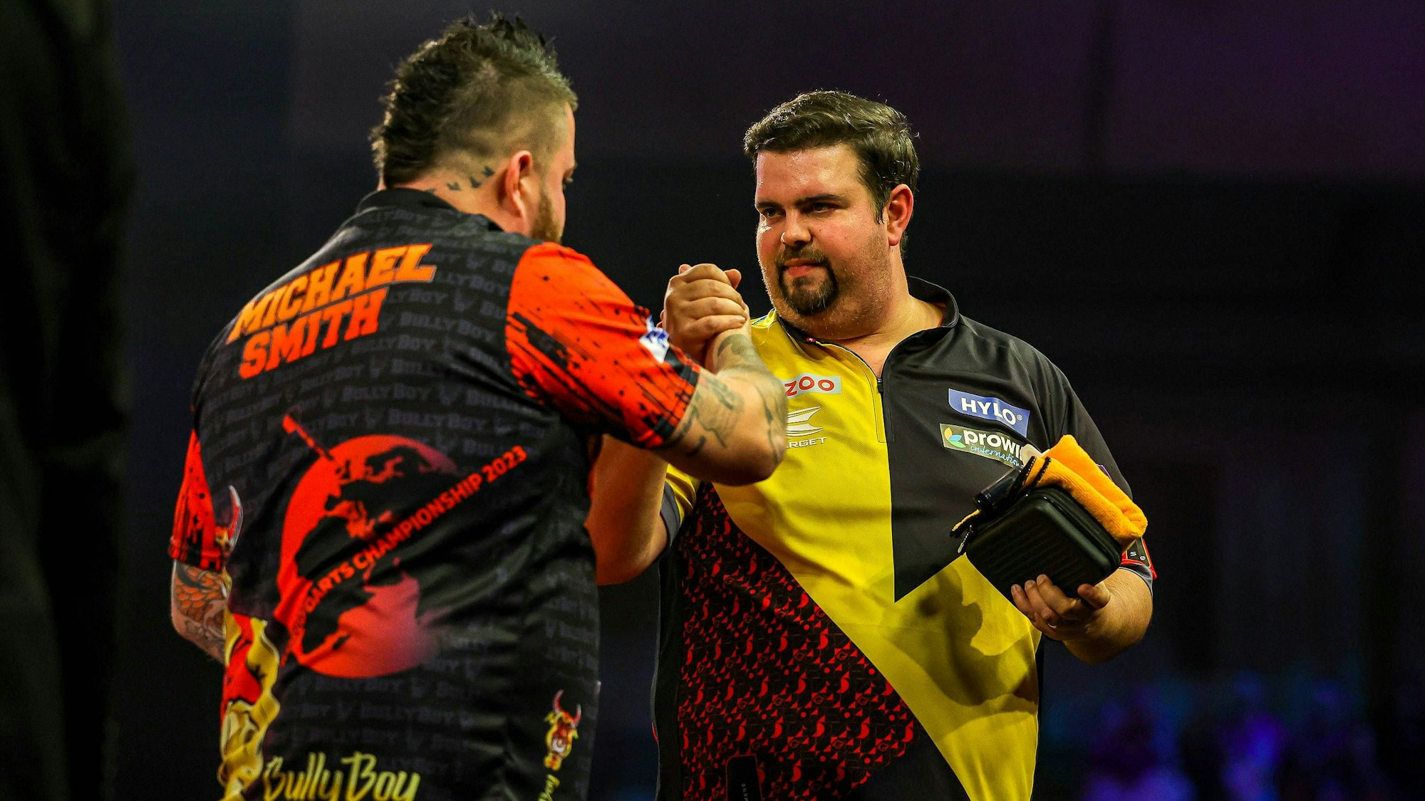 Die Darts-Spieler Gabriel Clemens und Michael Smith geben sich auf der Bühne die Hand.