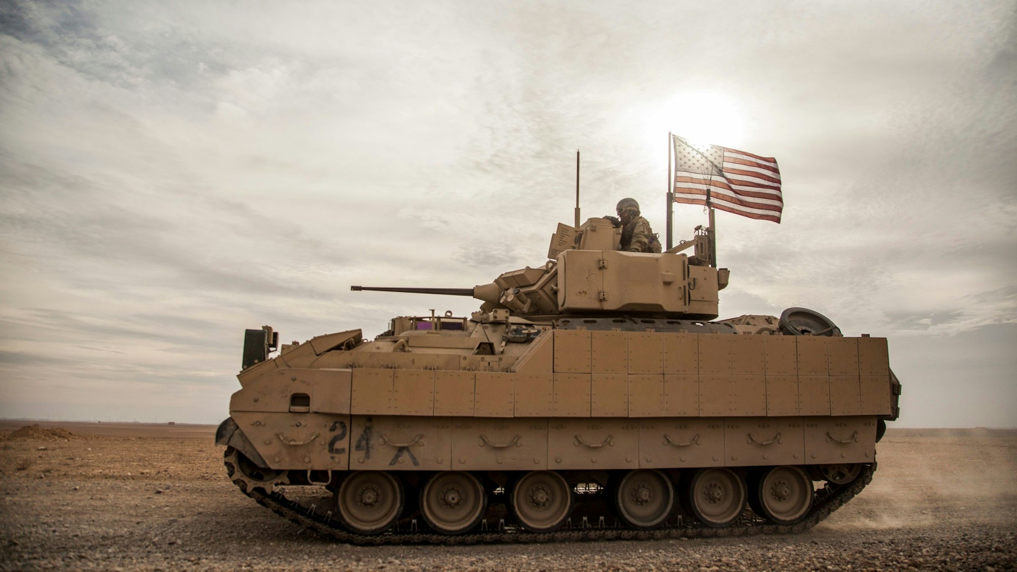 Amerikanische Soldaten fahren ein Bradley-Kampffahrzeug in der syrischen Wüste und hissen dabei eine USA-Flagge.