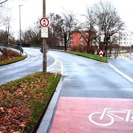 Eine Straße verzweigt sich, im Vordergrund ist ein großes Rad-Piktogramm zu sehen.