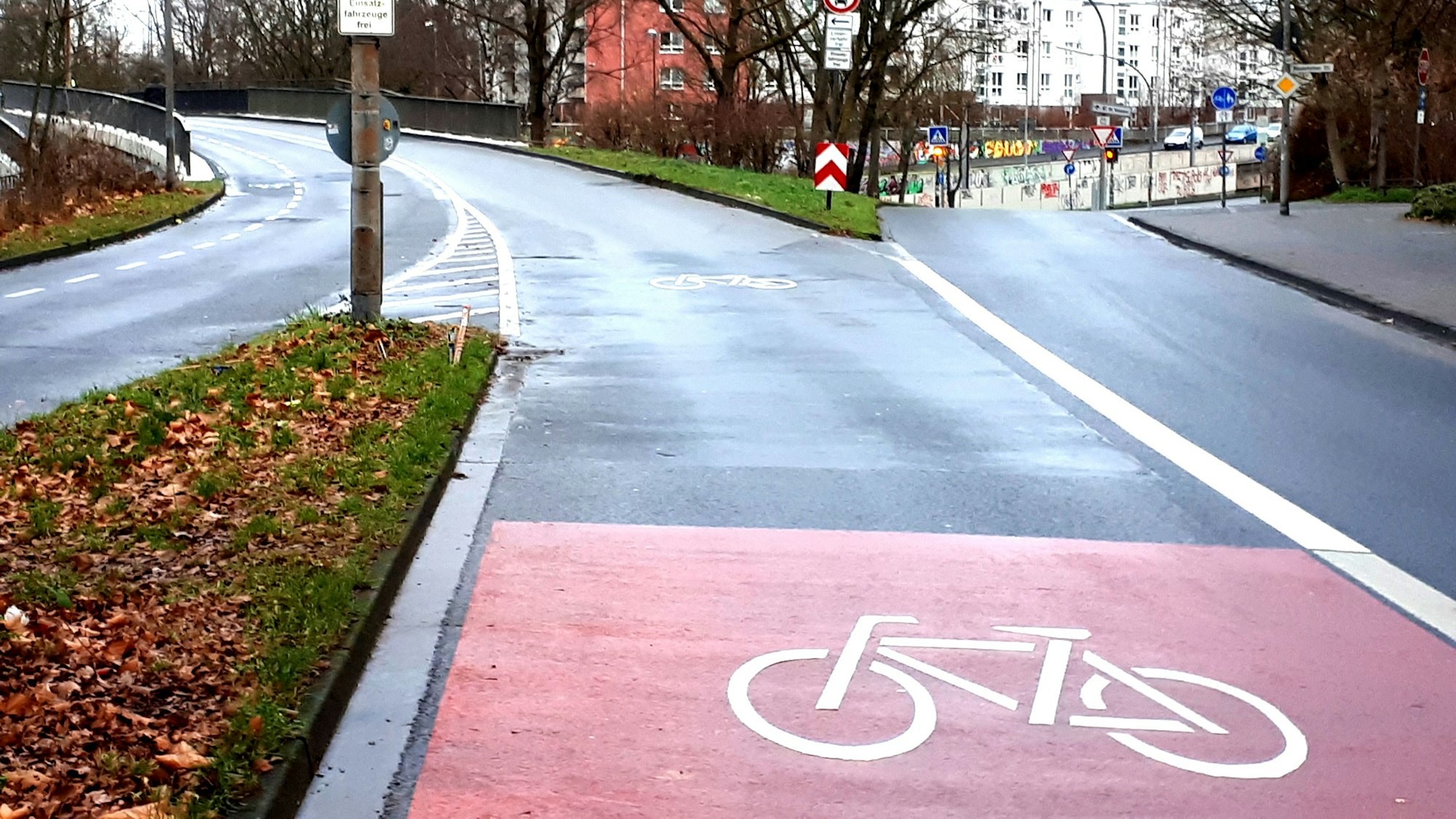 Eine Straße verzweigt sich, im Vordergrund ist ein großes Rad-Piktogramm zu sehen.