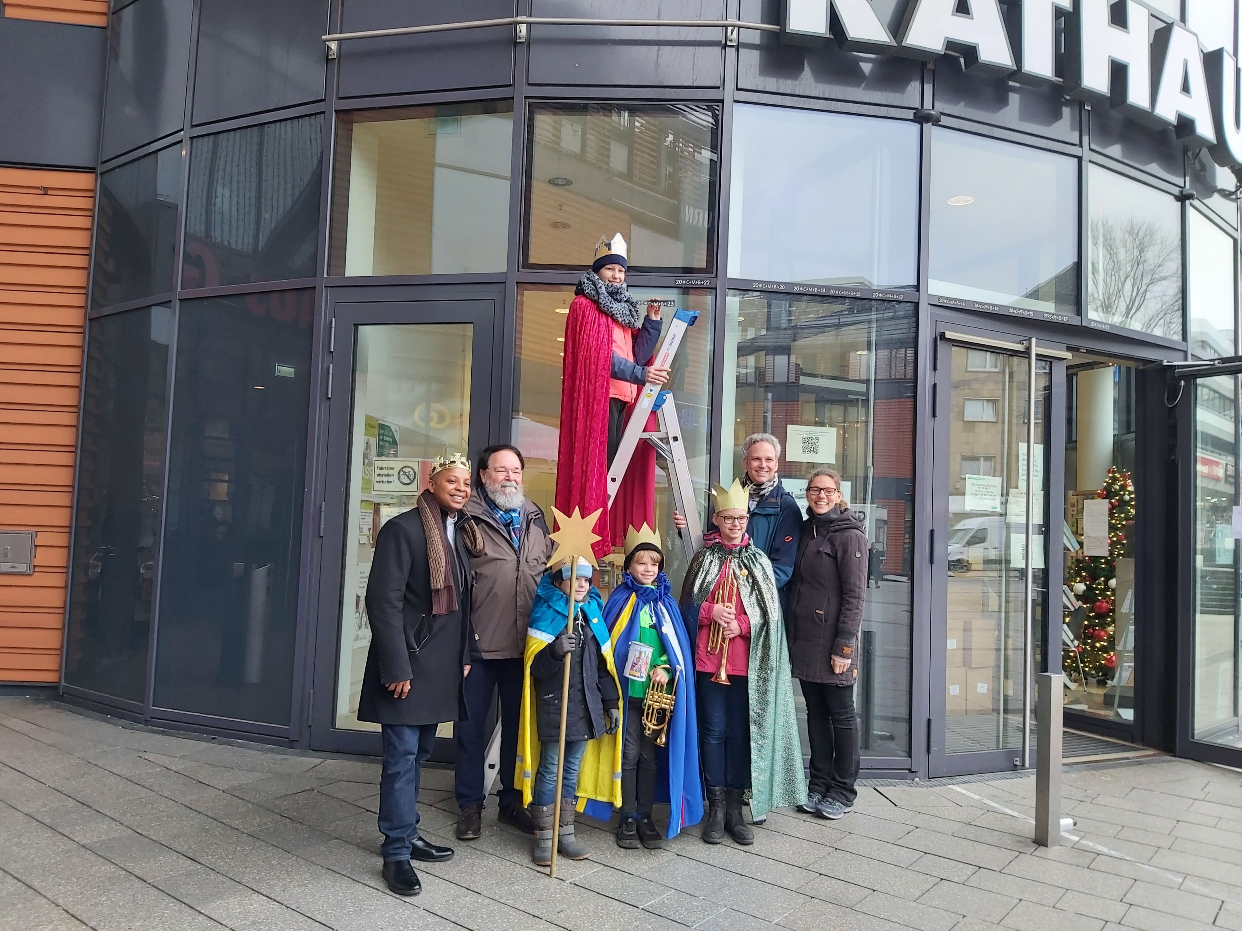 Die vier Sternsinger mit goldenen Kronen und Mänteln stehen mit Bürgermeister, Pater und ihren Eltern vor dem Rathaus.