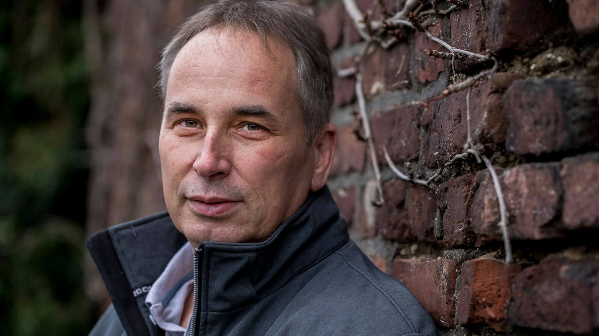 Wolfgang Stier guckt in die Kamera, er steht vor einer Backsteinmauer.