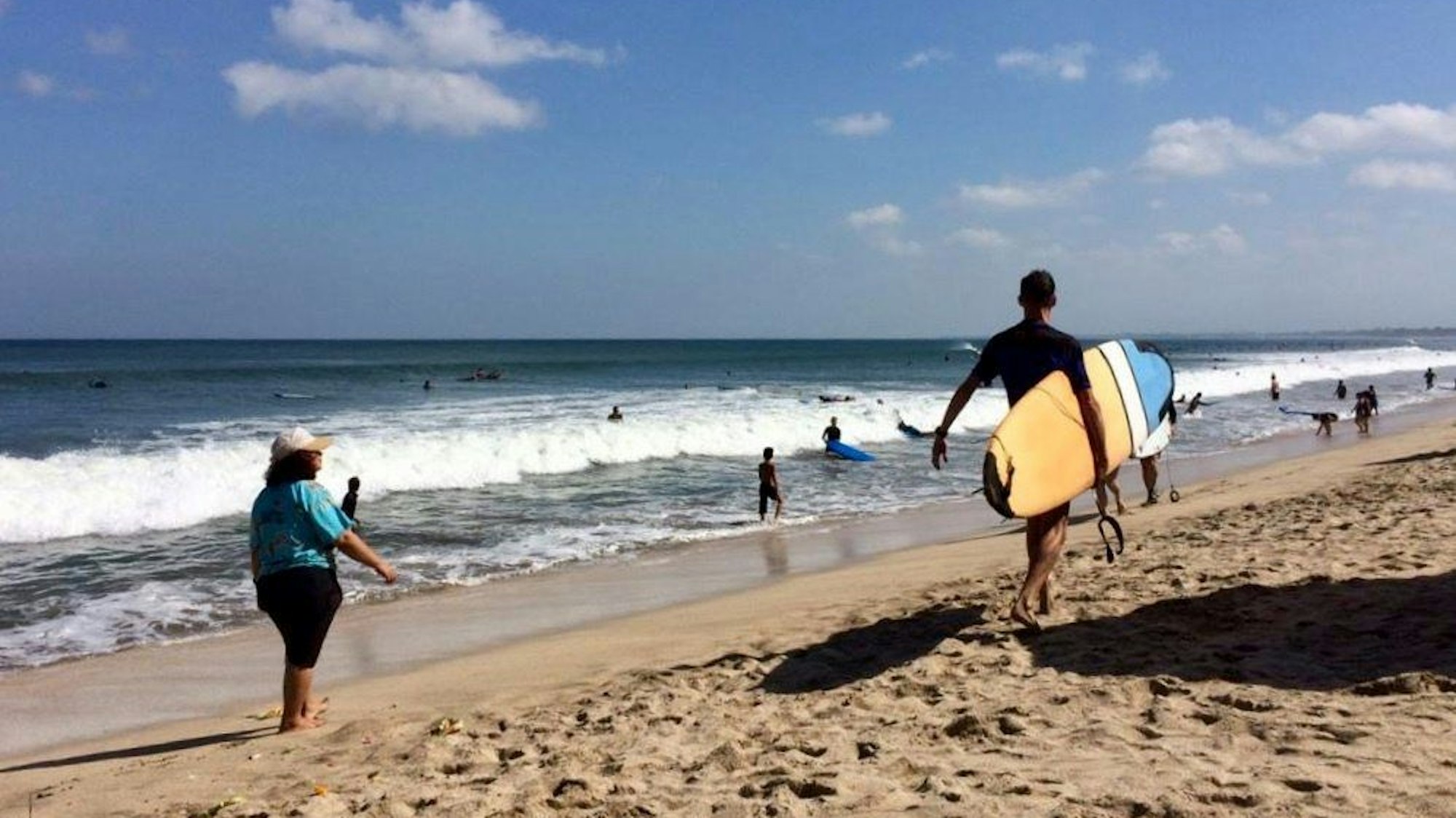 Ein Mann läuft mit einem Surfbrett am Strand entlang.