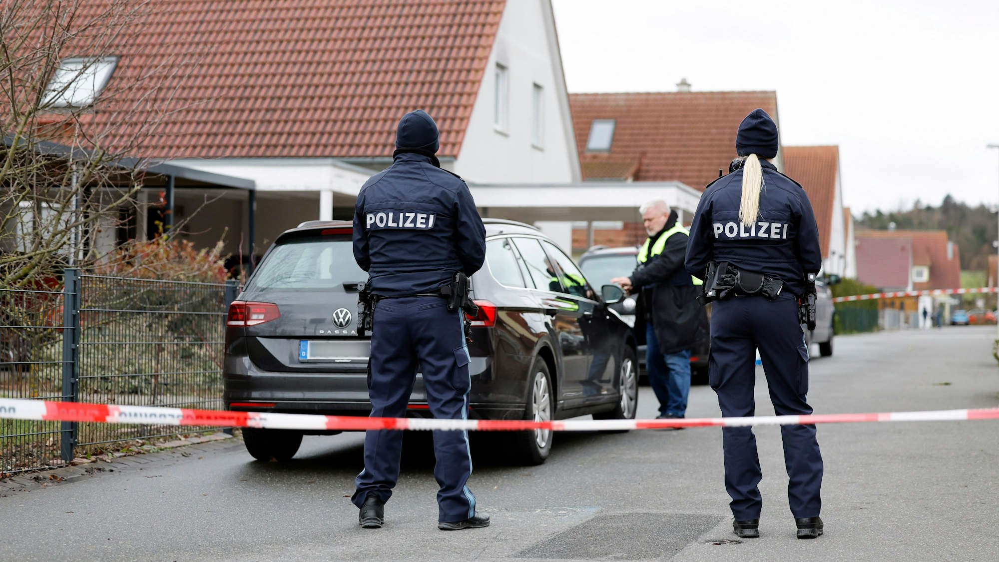 Polizeibeamte stehen in der Nähe des Wohnhauses, in dem es zu einer Gewalttat gekommen sein soll, man sieht sie von hinten.