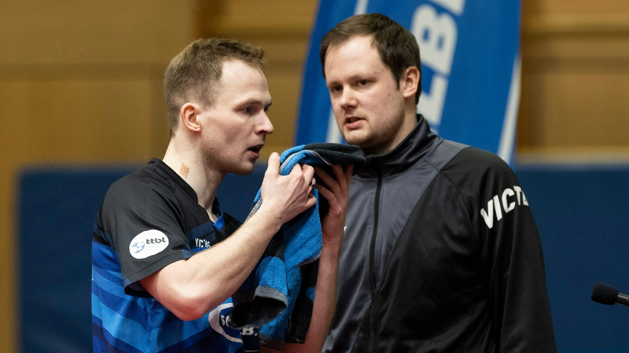 Schwalbe-Trainer Frederick Duda und sein Bruder und Spitzenspieler Benedikt Duda stehen in einer Sporthalle nebeneinander.