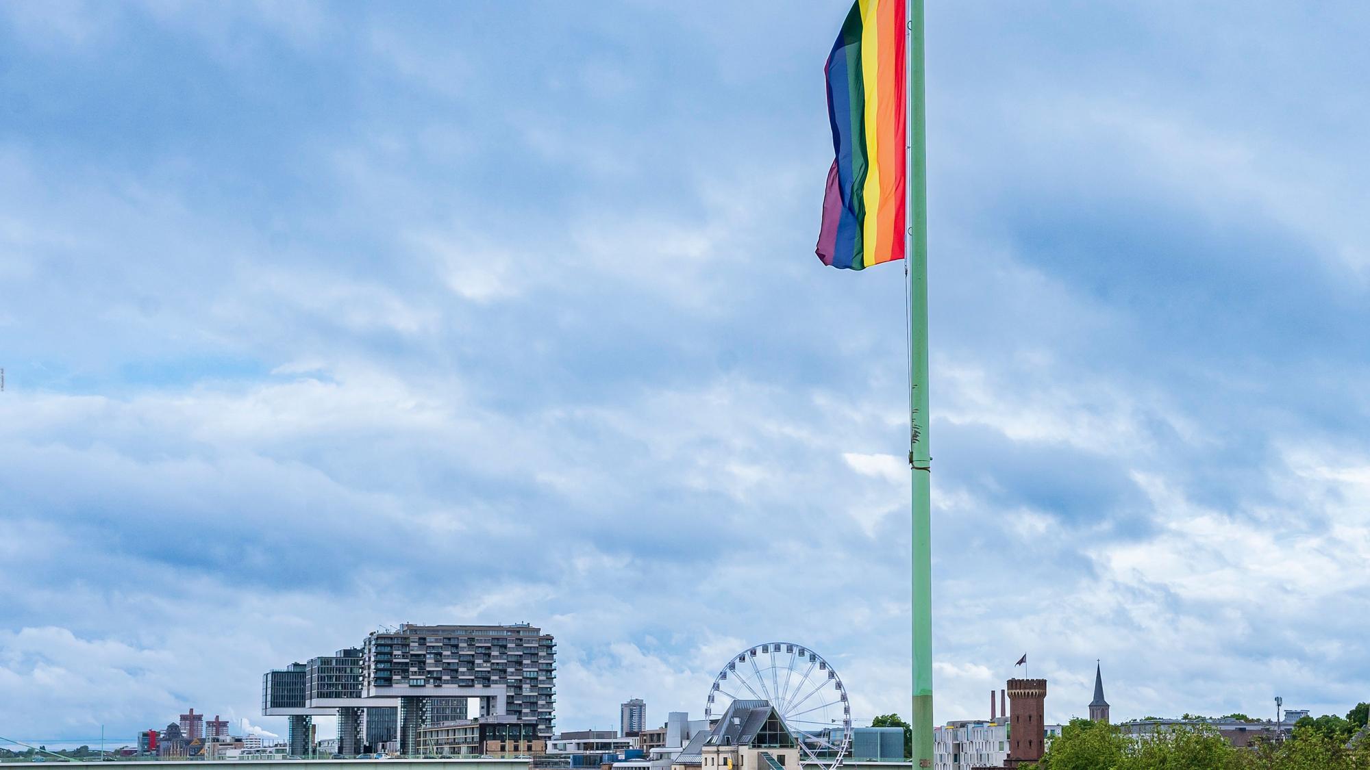Auf der Deutzer Brücke hängt eine Regenbogenflagge. Im Hintergrund die Kranhäuser und ein Riesenrad. Das Bild stammt aus dem Pride Month im Juni 2022.