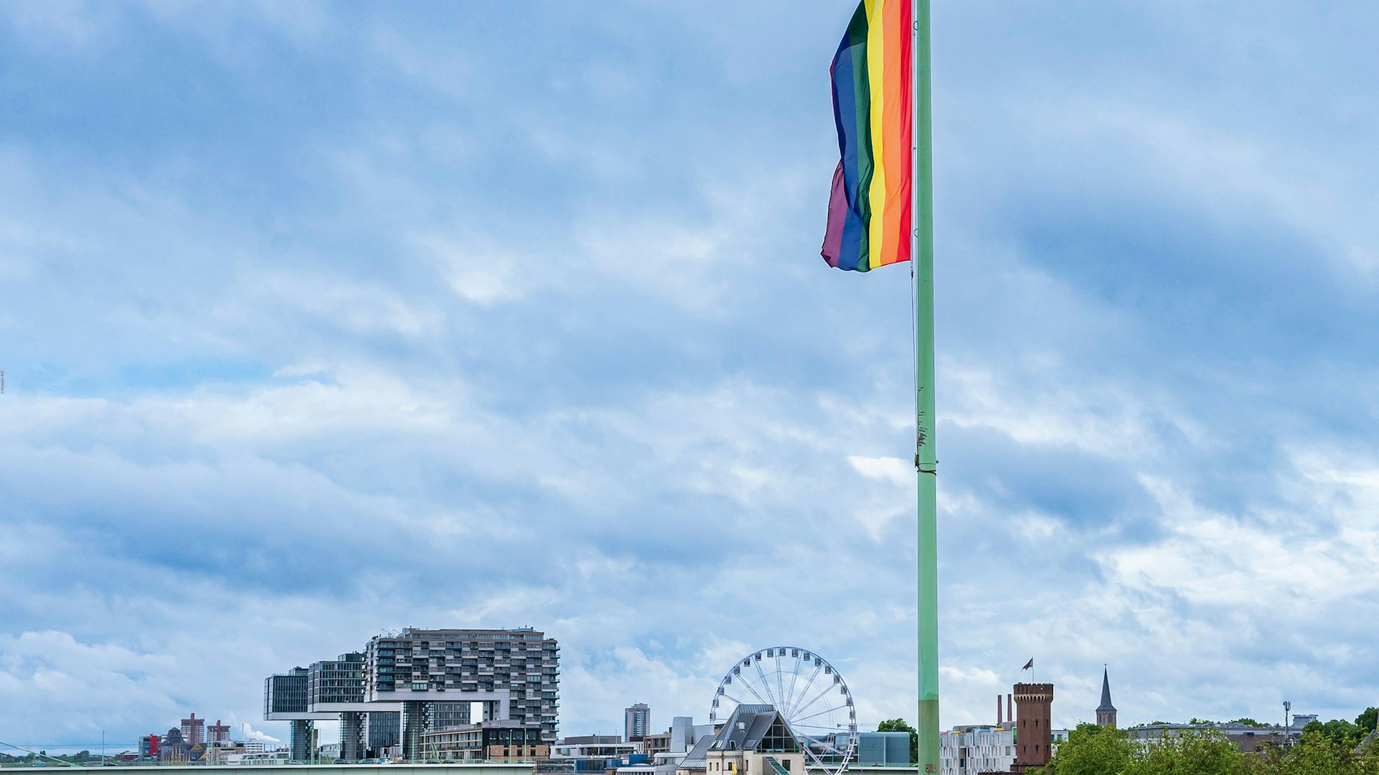 Auf der Deutzer Brücke hängt eine Regenbogenflagge. Im Hintergrund die Kranhäuser und ein Riesenrad. Das Bild stammt aus dem Pride Month im Juni 2022.