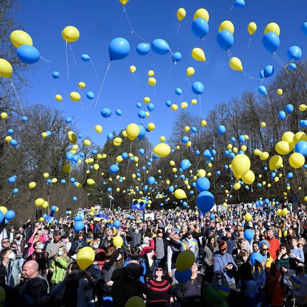 Hunderte Menschen lassen gelbe und blaue Luftballons in die Luft steigen.