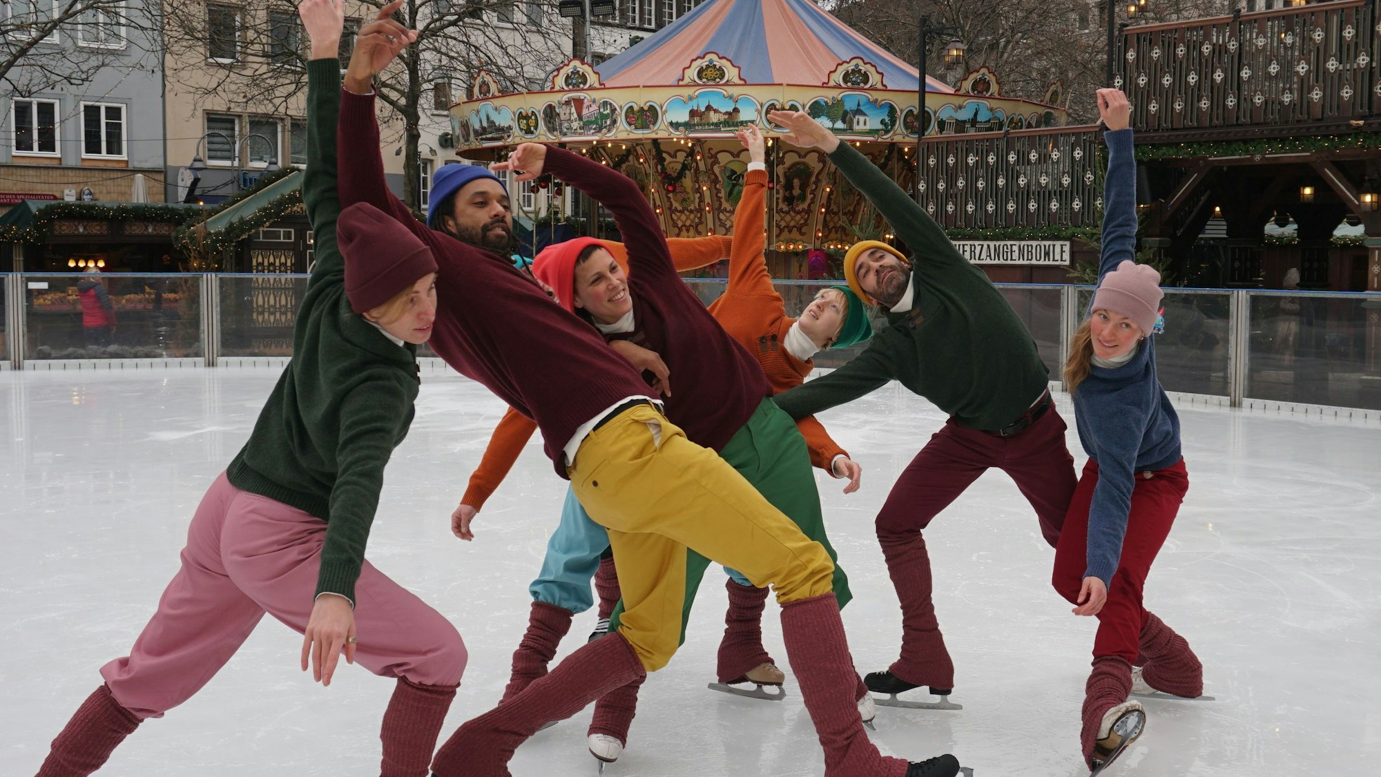 Eiskunstläufer in Aktion mit Weihnachtsmarkt im Hintergrund.