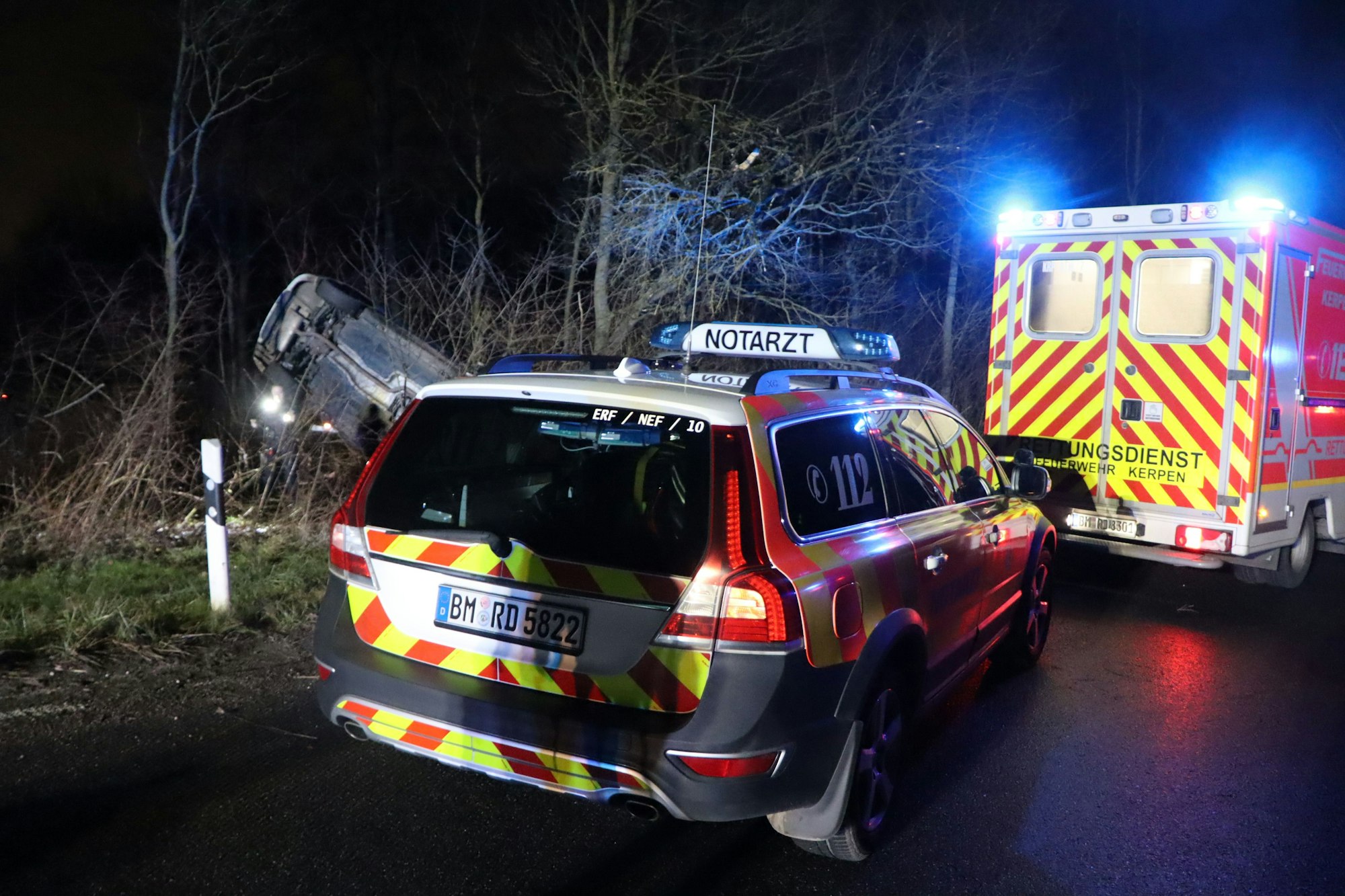 Zwei Rettungsdienst-Fahrzeuge stehen auf der Straße vor dem verunglückten Fahrzeug.