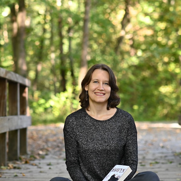 Elvira Zeißler sitzt mit einigen ihrer Bücher auf dem Schoß auf einem Holzsteeg.