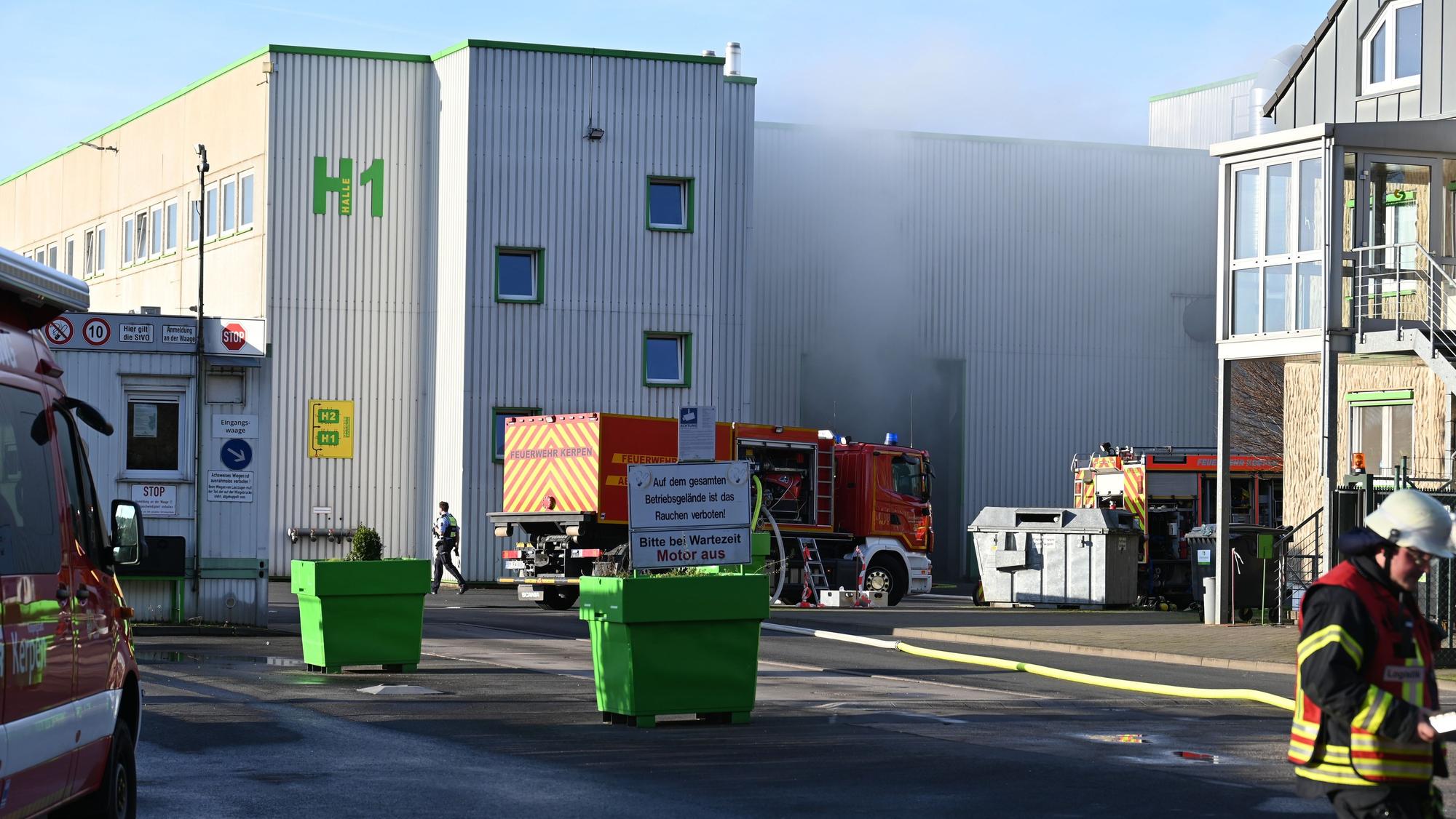 Feuer in einer Lagerhalle in Kerpen, Boelkestr. Rauch steigt auf, im Vordergrund stehen Feuerwehrwagen.