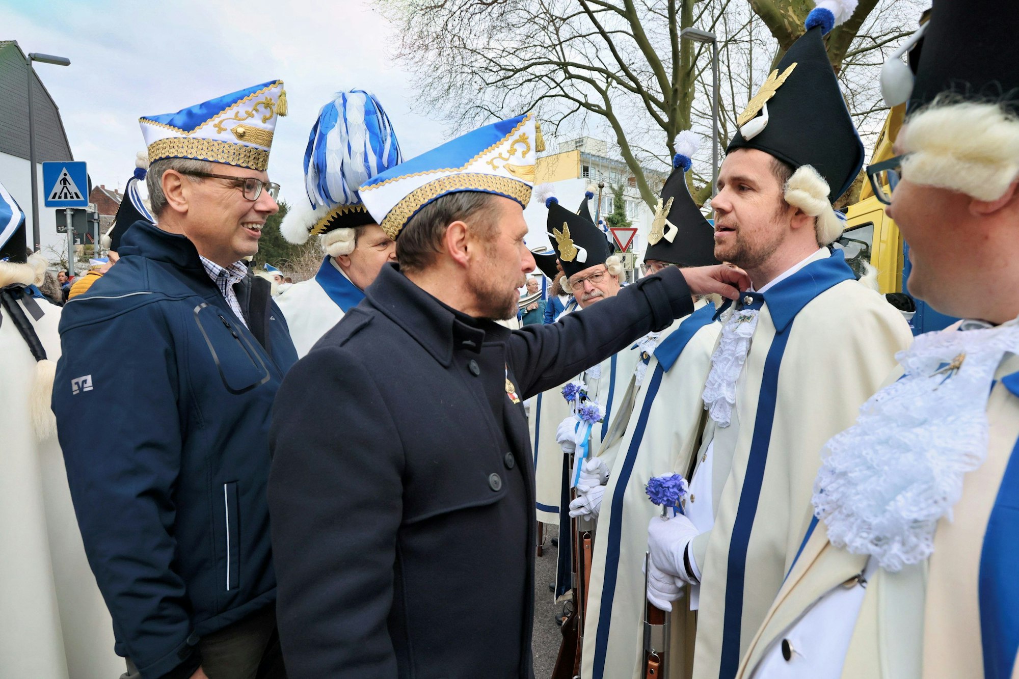 Oberbürgermeister Uwe Richrath steht, auf dem Kopf eine Narrenkappe, vor einem Funken und prüft den Sitz von dessen Uniform.