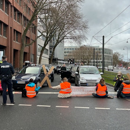 Aktivistinnen und Aktivisten der „Letzten Generation“ blockieren am Freitagmittag mit einer Sitzblockade die Cäcilienstraße, eine der zentralen Verkehrsachsen in der Kölner Innenstadt.