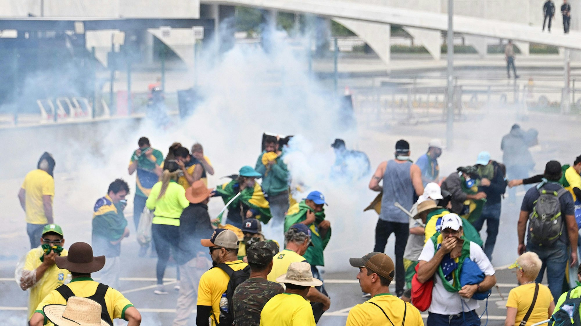 Menschen mit Kleidung in den Farben der Flagge Brasiliens stehen in dickem Rauch, einige halten sich Mund und Nase zu.