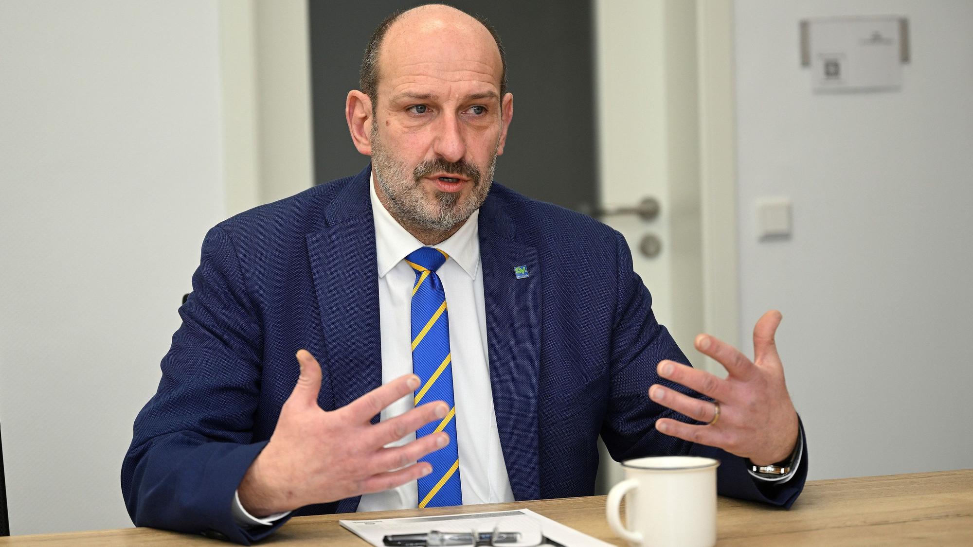 Overaths Bürgermeister Christoph Nicodemus sitzt an einem Tisch und gestikuliert.