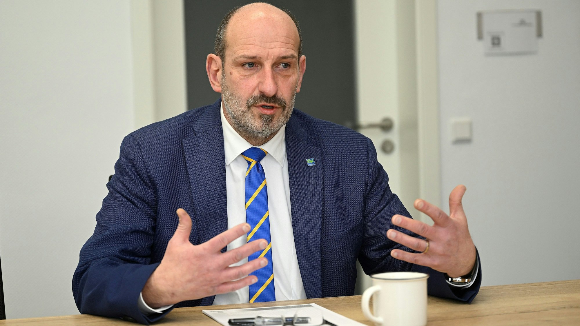 Overaths Bürgermeister Christoph Nicodemus sitzt an einem Tisch und gestikuliert.