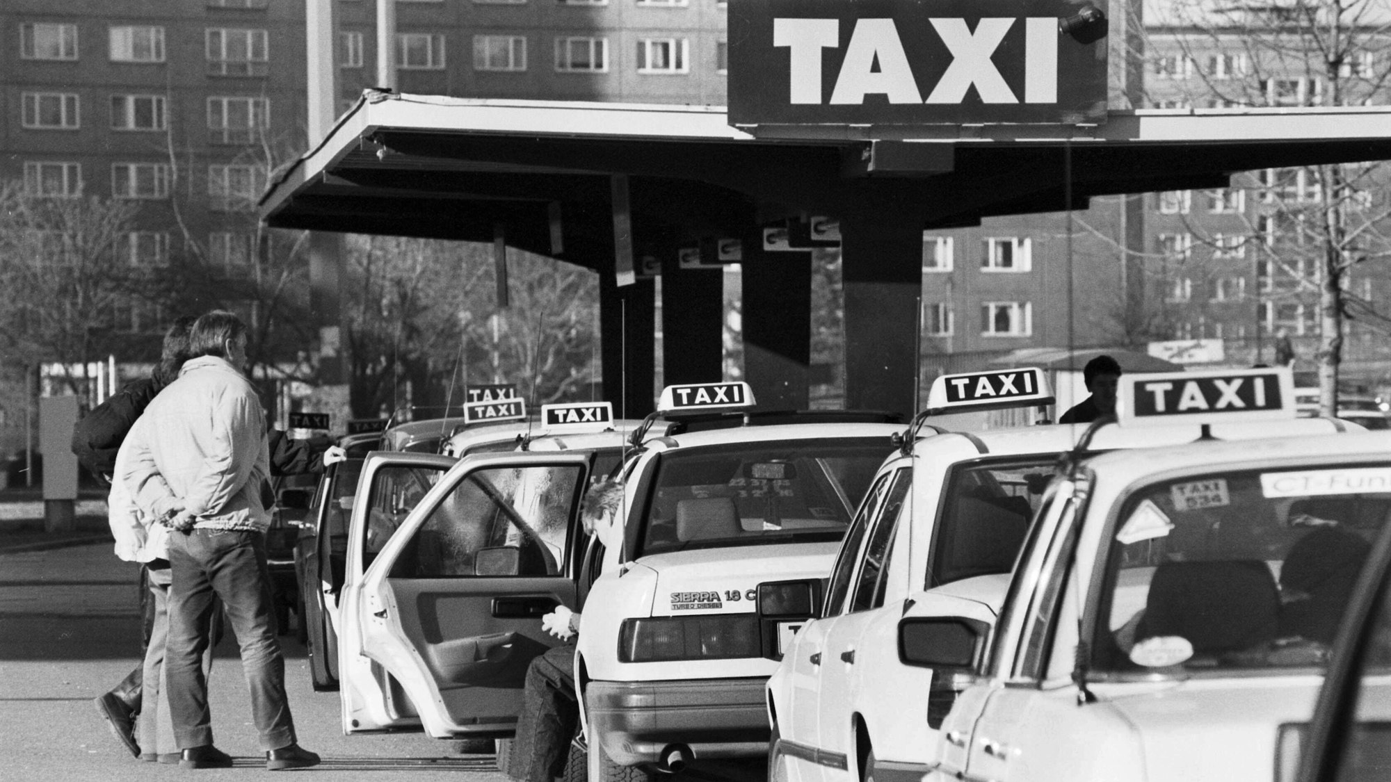 Schwarz-weiß-Bild mit zahlreichen, auf Fahrgäste wartenden Taxis