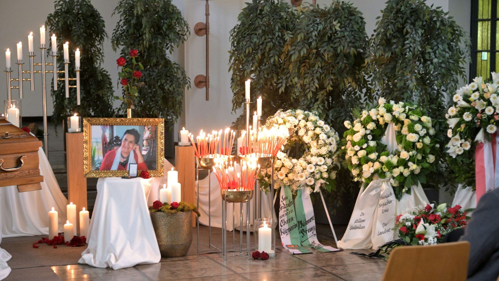 Blumen und Kerzen stehen neben dem Sarg und einem Bild von Philomena Franz.