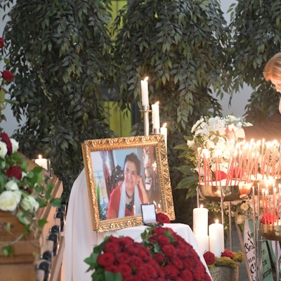 Zwei Frauen stehen vor dem Gold umrahmten und mit Blumen und Kerzen geschmückten Bild von Philomena Franz.