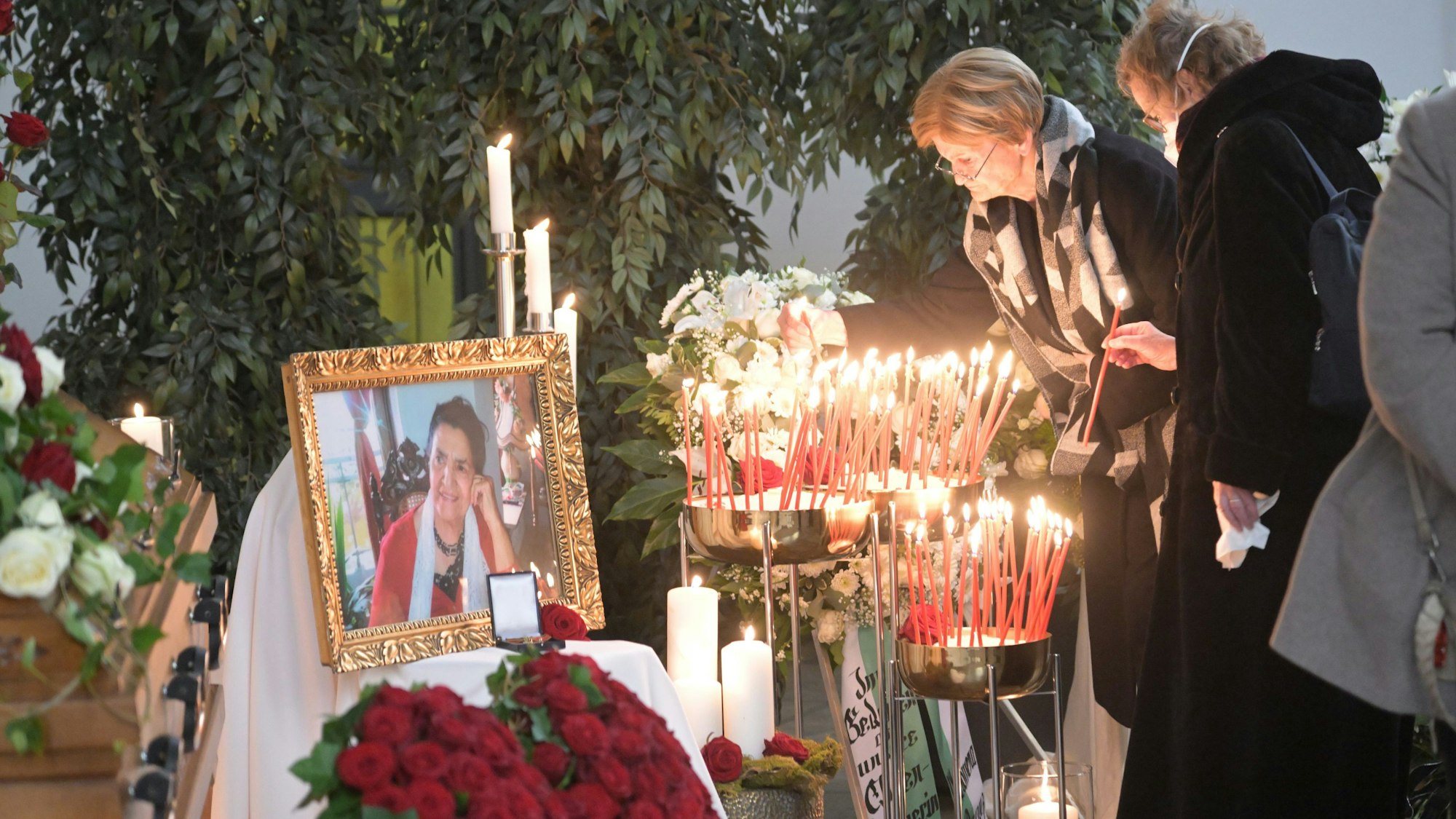 Zwei Frauen stehen vor dem Gold umrahmten und mit Blumen und Kerzen geschmückten Bild von Philomena Franz.