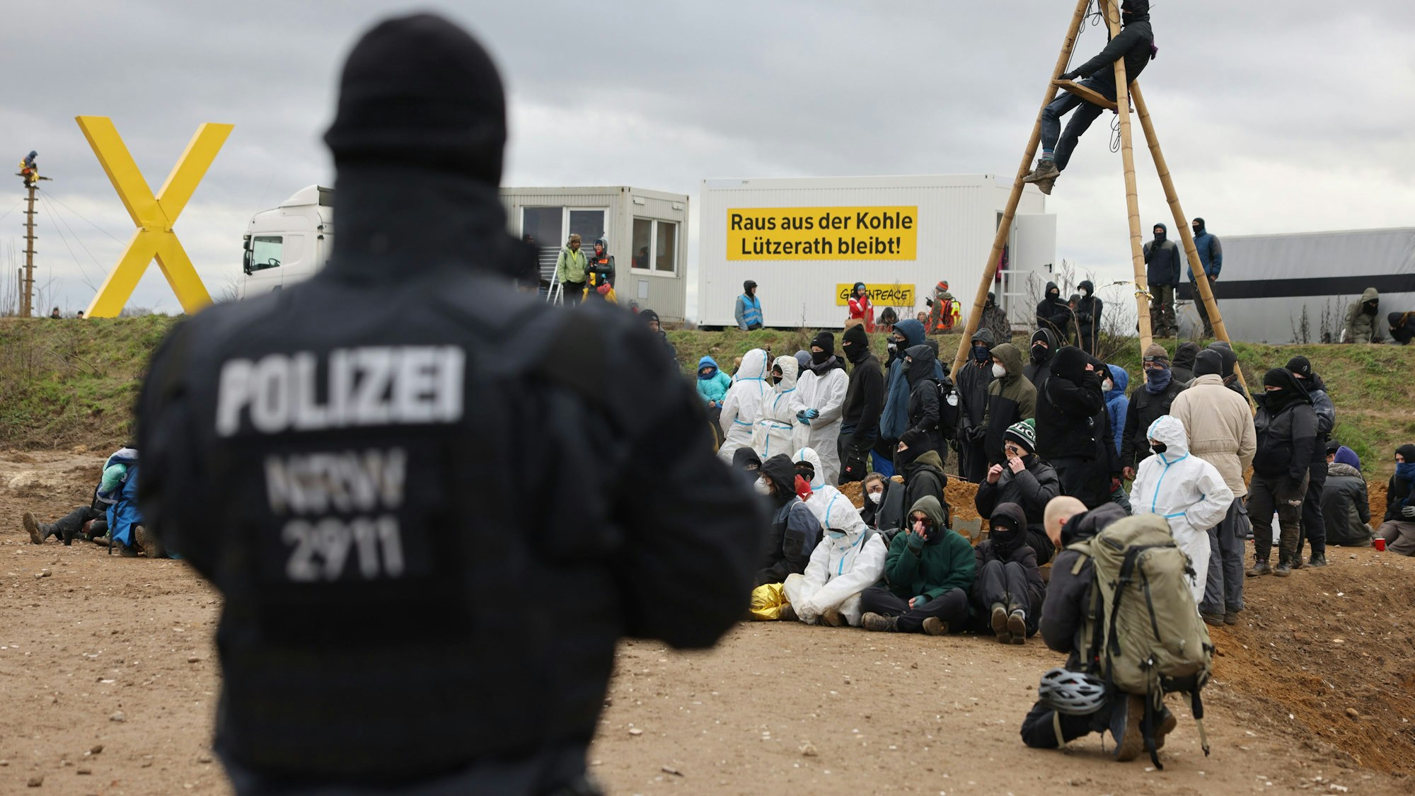 Ein Polizist beobachtet Klimaschutzaktivisten, die am Rand des Tagebaus sitzen. Das Dorf Lützerath soll zur Erweiterung des Braunkohletagebaus Garzweiler II abgebaggert werden.