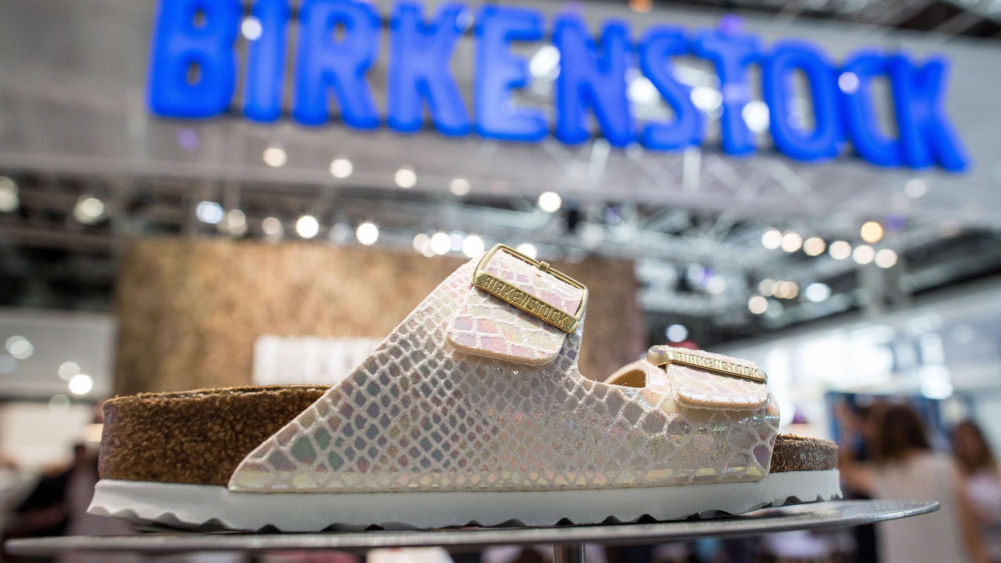 weiße Sandale in Lederoptik, Birkenstock-Logo im Hintergrund