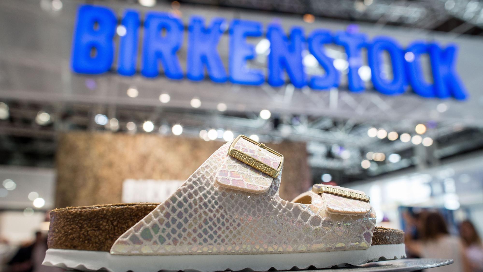 weiße Sandale in Lederoptik, Birkenstock-Logo im Hintergrund