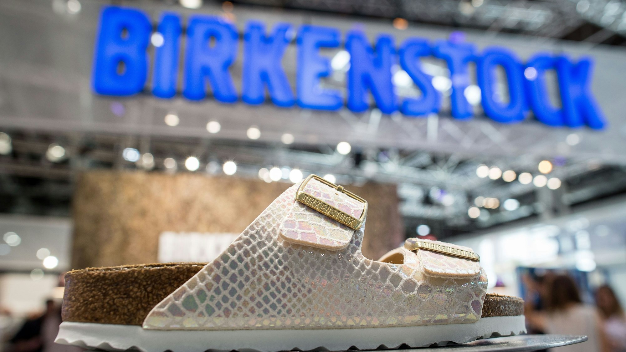 weiße Sandale in Lederoptik, Birkenstock-Logo im Hintergrund