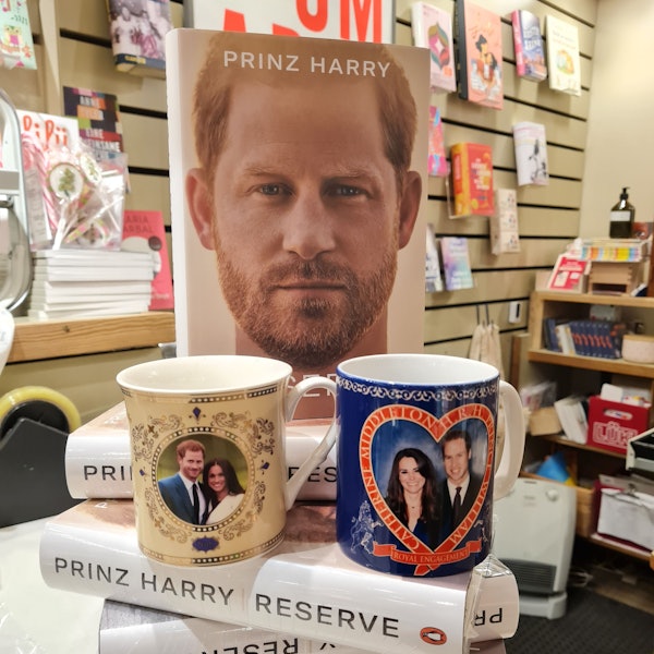 Auf einem kleinen Stapel des Buches von Prinz Harry steht eine Tasse mit dem Foto von Harry und Meghan und eine mit dem Foto von William und Kate.
