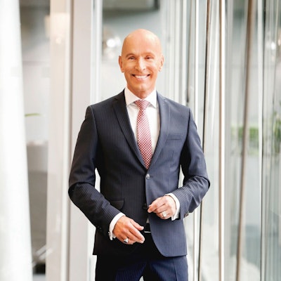 Michael Begasse steht vor einer Fensterfront und lächelt.