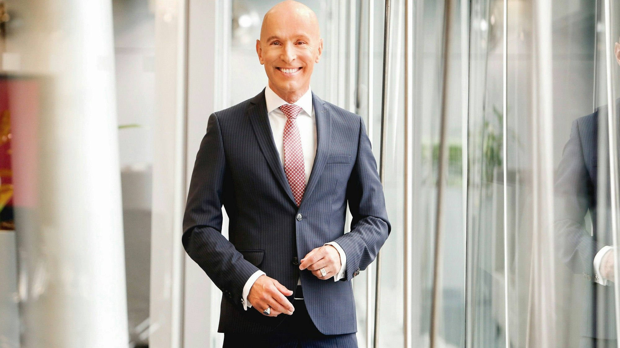 Michael Begasse steht vor einer Fensterfront und lächelt.