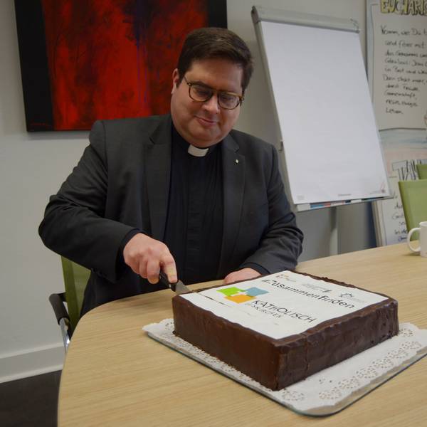 1Pfarrer Tobias Hopmann schneidet den Kuchen an, der das Logo der neuen pastoralen Einheit Euskirchen zeigt.
