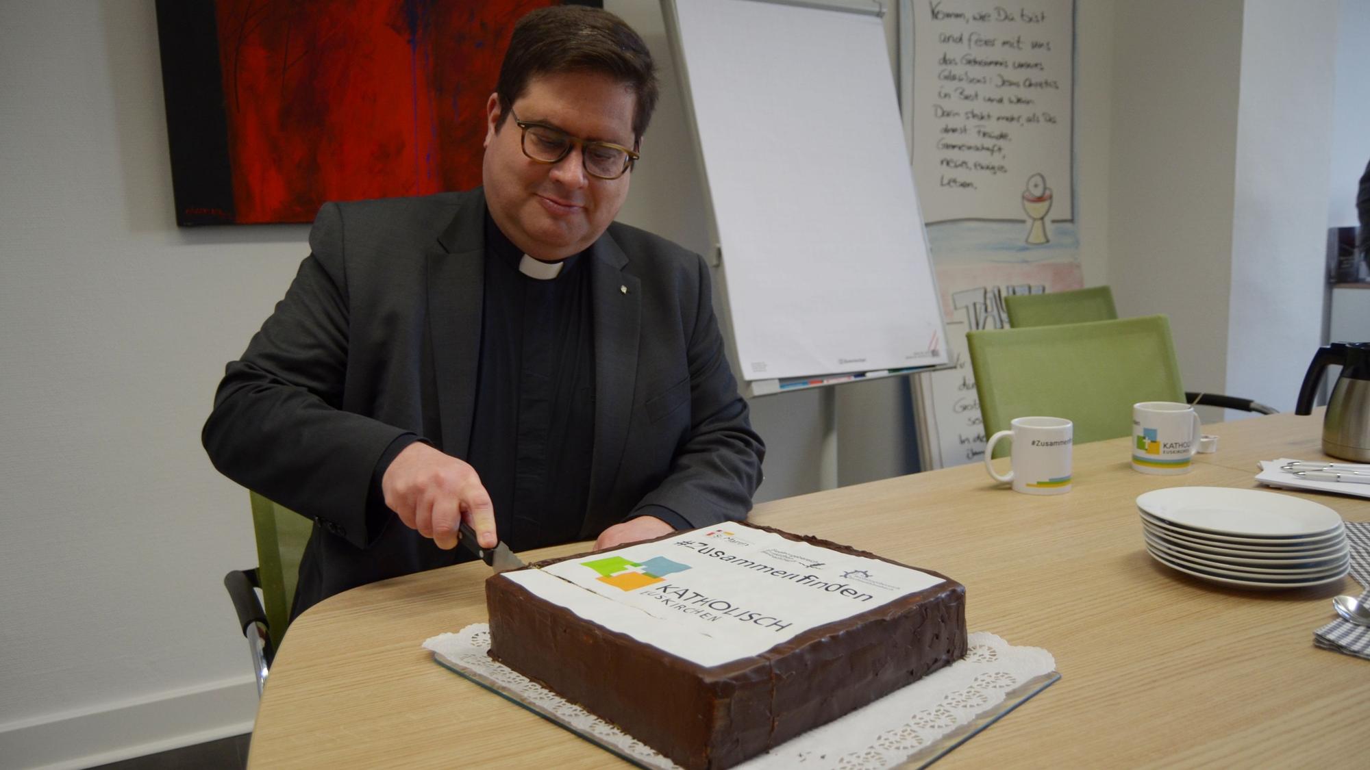 1Pfarrer Tobias Hopmann schneidet den Kuchen an, der das Logo der neuen pastoralen Einheit Euskirchen zeigt.