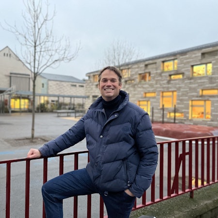 Thomas Heidbrink, der Schulpflegschaftsvorsitzender der GGS Hohe Straße steht am Zaun vor der Schule und lächelt.