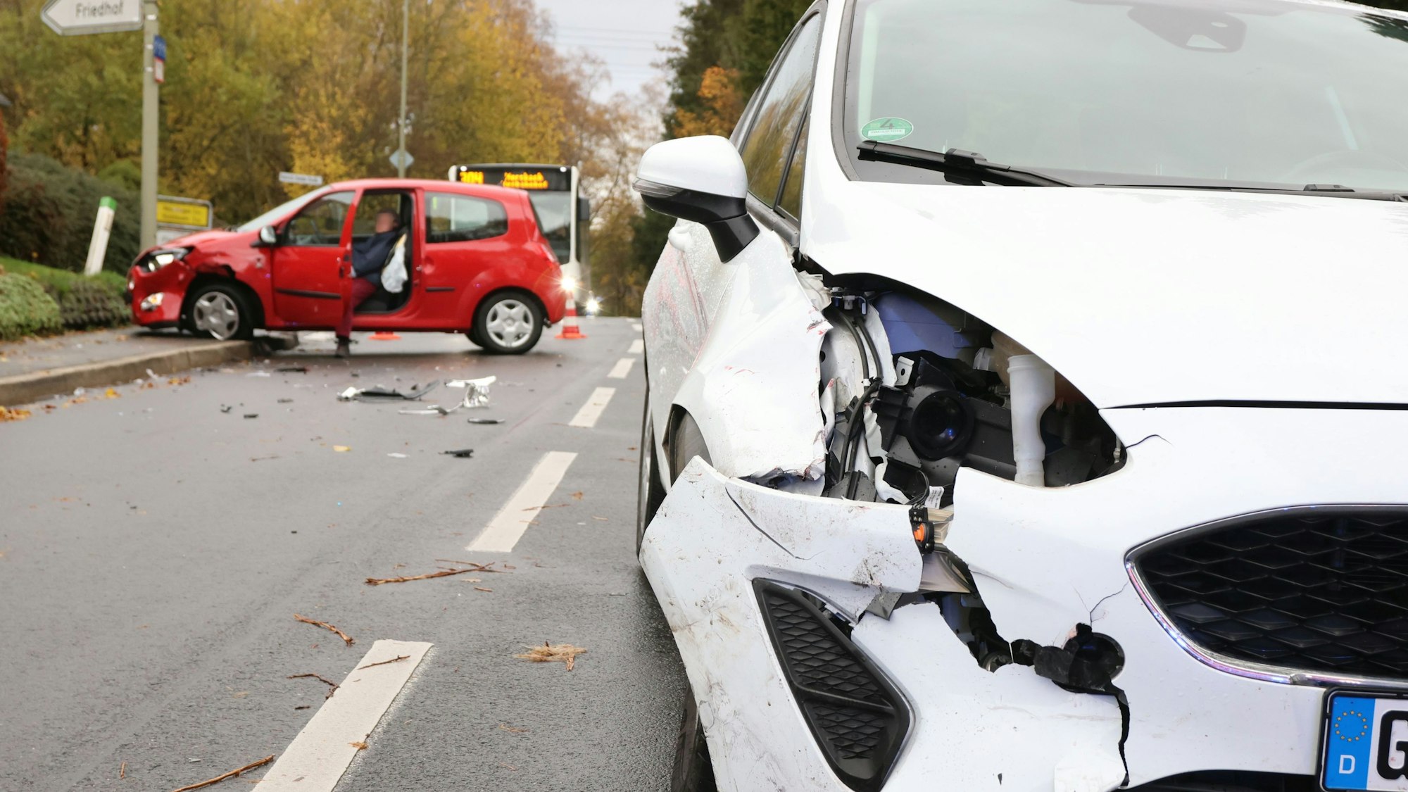 Ein beschädigter weißer Wagen steht nach einem Verkehrsunfall in Oberbantenberg mitten auf der Straße, der rote Unfall-Pkw im Hintergrund ist auf dem Fußgängerweg gefahren.