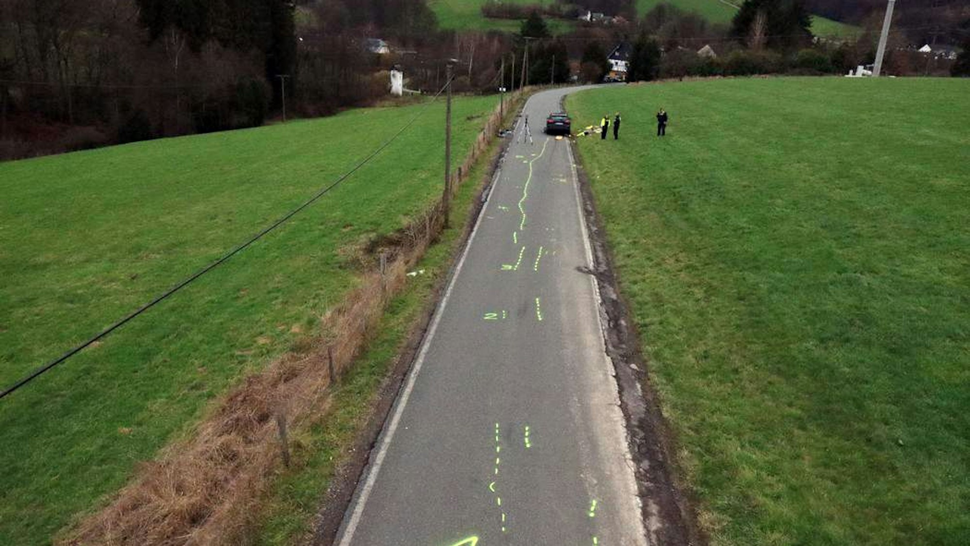 Mit Polizeikreide sind auf einer Straße die Brems- und weitere Spuren eines Unfallautos markiert, im Hintergrund ist das Unfallauto zu sehen.