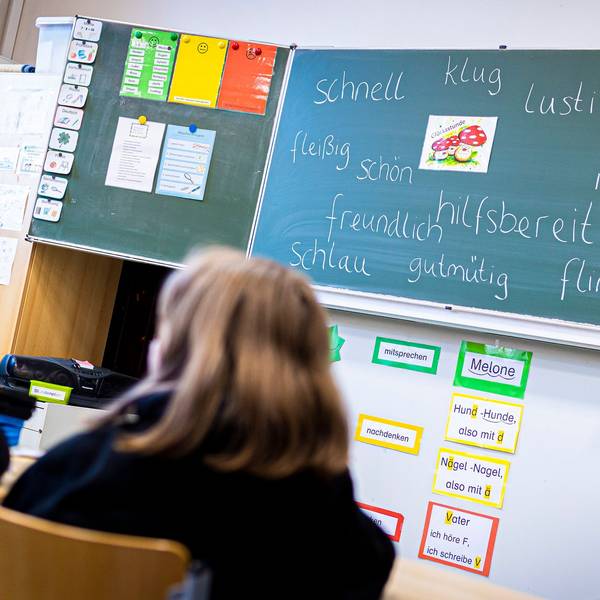 Drei Kinder in Schwarz sitzen in einem Klassenraum vor einer Tafel, die mit Adjektiven beschrieben ist.